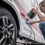 Caucasian Technician Trying To Fix RV Travel Trailer Electric Hookup Problem Looking Inside Outside Compartment.