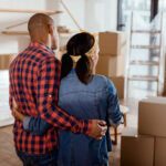 rear view of couple looking at new home with cardboard boxes